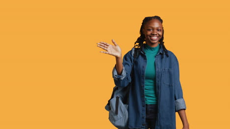 Cheerful-student-witch-school-rucksack-doing-greeting-hand-gesture