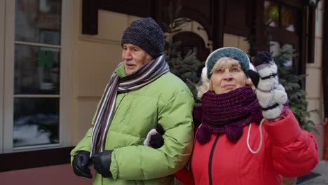 Front-view-of-senior-couple-tourists-man-woman-walking,-talking,-gesturing-in-winter-holiday-city