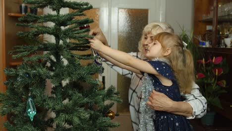 Children-girl-with-grandparents-couple-decorating-artificial-Christmas-pine-tree-at-old-fashion-home