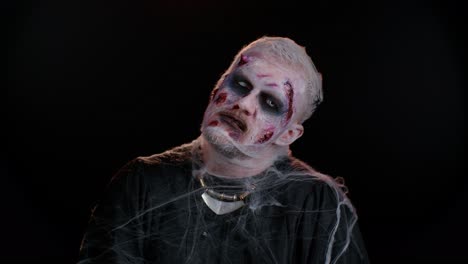 Sinister-man-with-horrible-scary-Halloween-zombie-makeup-in-convulsions-making-faces-trying-to-scare