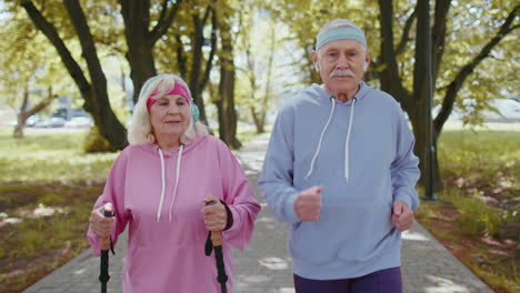 Cheerful-senior-old-couple-grandfather,-grandmother-training-Nordic-walking,-running-in-summer-park