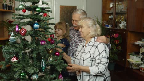 Kleines-Mädchen-Mit-Großmutter-Und-Großvater,-Die-Einen-Künstlichen-Weihnachtsbaum-Mit-Spielzeug-Dekorieren