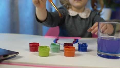 Kind-Schulmädchen-Begeistert-Zeichnen-Mit-Pinsel,-Farben-Zu-Hause-Sitzen-Am-Tisch-Mit-Laptop