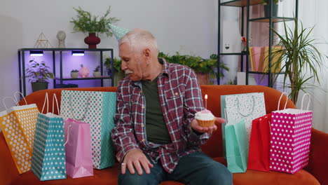 Happy-senior-elderly-grandfather-man-celebrating-birthday-party,-makes-wish-blowing-burning-candle