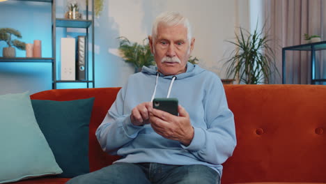 Senior-Großvater-Zu-Hause-Mit-Smartphone-Tippen-Und-Surfen,-Wow,-Ja,-Fand-Einen-Großen-Gewinn-Heraus,-Feiern