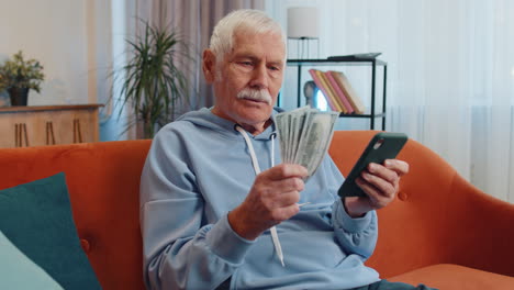Lächelnder,-Glücklicher-älterer-Großvater,-Der-Geld-Zählt,-Bargeld-Nutzt-Smartphone,-Einkommen,-Spart,-Lottogewinn