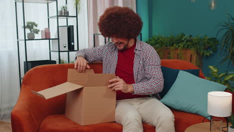 Happy-young-man-shopper-unpacking-cardboard-box-delivery-parcel-online-shopping-purchase-at-home