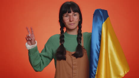 Young-woman-holding-Ukraine-national-flag,-showing-victory-sign-against-war,-hoping-success-win