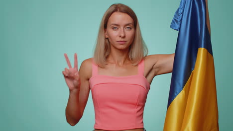 Woman-holding-Ukraine-national-flag,-showing-victory-sign-against-war,-hoping-for-success-and-win