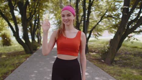 Athletic-fitness-runner-girl-waving-hi-hello-with-her-palm-greeting-with-hospitable-friendly-smile