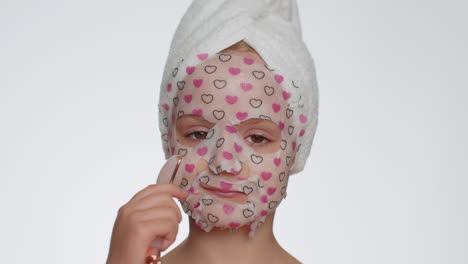 Lovely-young-smiling-child-girl-applying-cosmetic-moisturizing-face-mask,-use-massage-roller