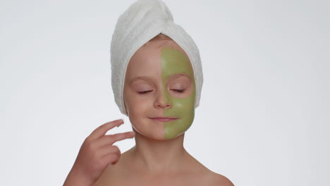 Schönes-Lächelndes-Kind-Mit-Handtuch-Auf-Dem-Kopf,-Das-Eine-Reinigende,-Feuchtigkeitsspendende-Grüne-Maske-Auf-Das-Gesicht-Aufträgt