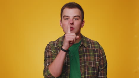 Young-man-presses-index-finger-to-lips-makes-silence-gesture-sign-do-not-tells-secret,-shh-be-quiet