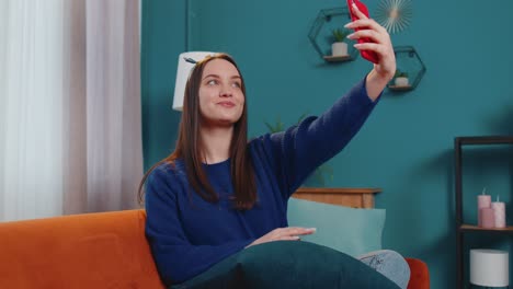 Woman-on-sofa-at-home-with-smartphone-taking-selfie-on-mobile-phone-cam,-virtual-video-call-online