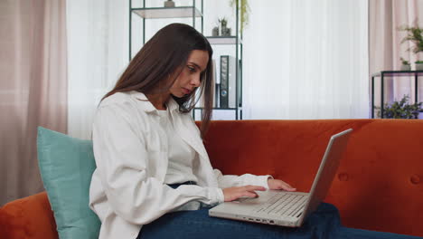 Young-woman-freelancer-sitting-on-sofa-closing-laptop-pc-after-finishing-work-in-living-room-at-home