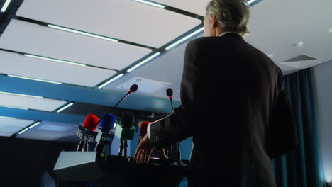 Female-politician-makes-an-announcement,-answers-journalists-questions-and-gives-interview-for-media.-Confident-representative-of-the-European-Union-during-press-conference.-Backdrop-with-EU-flags.