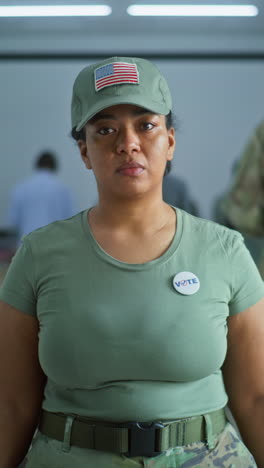 Portrait-of-female-soldier,-United-States-of-America-elections-voter.-Woman-in-camouflage-uniform-stands-in-polling-station-and-looks-at-camera.-Background-with-voting-booths.-Concept-of-civic-duty.