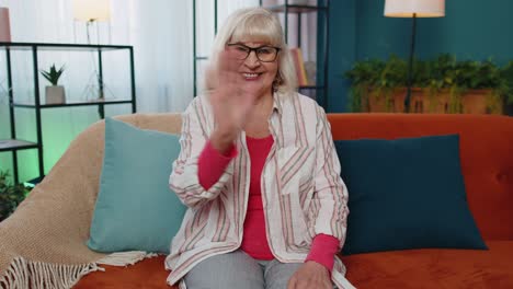 Senior-grandmother-smiling-friendly-at-camera,-waving-hands-gesturing-hello,-hi,-greeting-at-home