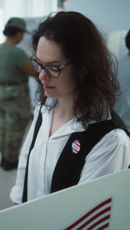 Portrait-of-female-soldier,-United-States-of-America-elections-voter.-Woman-in-camouflage-uniform-stands-in-polling-station-and-looks-at-camera.-Background-with-voting-booths.-Concept-of-civic-duty.