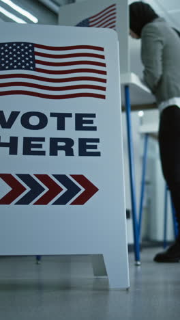 Vote-here-sign-on-the-floor.-Diverse-American-citizens-vote-in-booths-in-polling-station-office.-National-Elections-Day-in-the-United-States.-Political-races-of-US-presidential-candidates.-Civic-duty.
