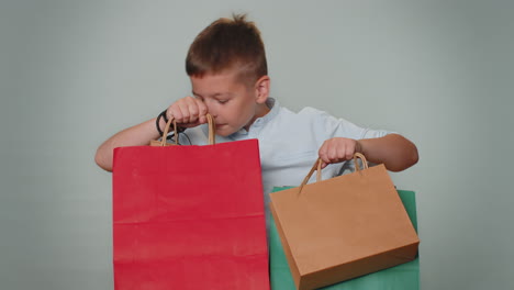 Toddler-boy-showing-shopping-bags,-advertising-discounts,-smiling-looking-amazed-with-low-prices