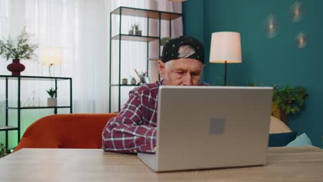 Senior-grandfather-man-using-laptop-computer,-typing-at-home-room,-looking-at-camera,-smiling