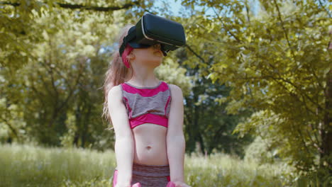 Athletic-child-in-VR-headset-helmet-making-fitness-workout-exercises-with-dumbbells-outdoors-in-park