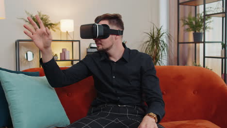 Der-Junge-Mann-Verwendet-Zu-Hause-Eine-Virtual-Reality-Headset-Brille-Und-Genießt-Das-Videokonzept,-Bei-Dem-Er-Die-Hände-In-Der-Luft-Bewegt