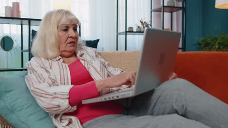 Stressed-upset-senior-grandmother-woman-working-on-laptop-computer,-received-bad,-loss-news-at-home