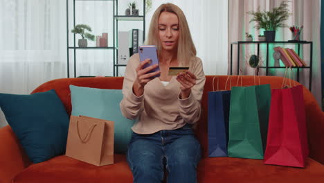 Happy-shopaholic-young-woman-sitting-with-shopping-bags-making-online-payment-with-credit-card