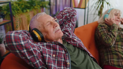 Happy-senior-family-grandparents-man-woman-in-headphones-listening-music-relaxing-on-couch-at-home