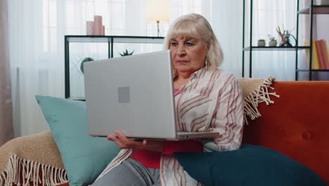Senior-grandmother-woman-using-laptop-computer,-typing-at-home-room,-looking-at-camera,-smiling