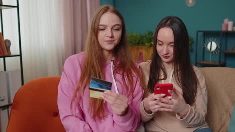 Cheerful-girls-friends-using-credit-bank-card-and-smartphone-while-transferring-money,-purchases