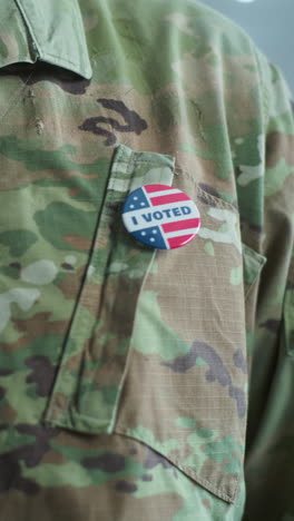 Close-up-of-military-man-putting-on-badge-with-American-flag-logo-and-inscription-I-Voted.-US-citizen,-voter-at-polling-station-during-elections.-National-Election-Day-in-the-United-States-of-America.