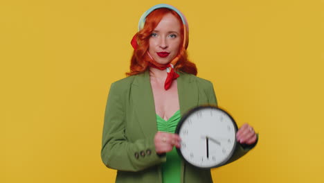 Redhead-young-woman-showing-time-on-wall-office-clock,-ok-thumb-up-approve-pointing-finger-at-camera