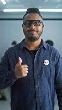 Nervous-African-American-male-voter-chooses-which-presidential-candidate-to-vote-for-in-voting-booth,-looks-at-camera.-US-citizen-at-polling-station-during-Election-Day-in-the-United-States-of-America