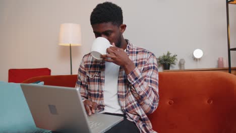 Young-man-using-laptop-computer-lying-on-sofa-at-home-working,-online-shopping-from-home-office