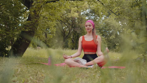 Mujer-Joven-Sentada-En-Una-Alfombra-En-Posición-De-Loto,-Relajándose,-Practicando-Meditación-De-Yoga-En-El-Parque-De-La-Ciudad