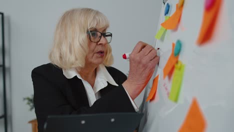 Ältere-Alte-Geschäftsfrau-Trainer-Konferenzsprecher-Analysieren-Infografiken-Zeichnen-Auf-Büro-Whiteboard