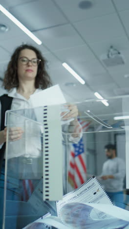 Diverse-voters,-American-people-vote-for-future-president-in-voting-booths-at-polling-station.-Caucasian-woman-puts-ballot-in-box.-National-Election-Day-in-the-United-States-of-America.-Slow-motion.