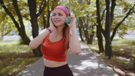 Sport-runner-pretty-girl-training-exercise-listening-music-on-headphones-dancing-having-fun-in-park