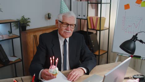 Älterer-Alter-Geschäftsmann-Feiert-Geburtstag-Im-Büro-Und-Hält-Einen-Kleinen-Kuchen-Mit-Kerzen-In-Der-Hand,-Um-Sich-Etwas-Zu-Wünschen