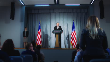 President-of-USA-answers-journalists-questions-and-gives-interview.-Confident-American-republican-politician-delivers-successful-speech-to-supporters-at-press-conference.-Backdrop-with-American-flags.