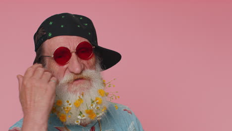Close-up-cheerful-stylish-senior-flowered-beard-man-wearing-sunglasses,-charming-smile-on-pink-wall
