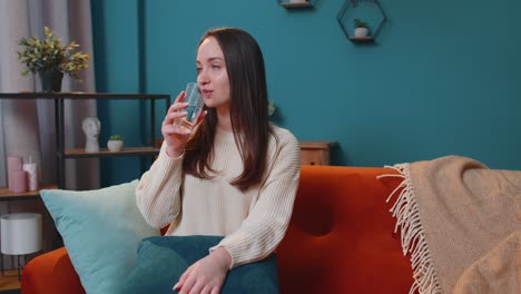 Thirsty-one-young-woman-sitting-at-home-holding-glass-of-natural-aqua-make-sips-drinking-still-water