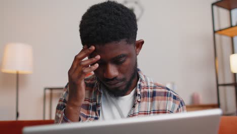 Afroamerikanischer-Mann-Sitzt-Auf-Dem-Sofa-Und-öffnet-Seinen-Laptop-PC,-Während-Er-Im-Wohnzimmer-Zu-Hause-Online-Mit-Der-Arbeit-Beginnt
