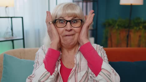 Wow,-excited-amazed-senior-old-grandmother-raising-hands-in-surprise-looking-at-camera-with-big-eyes