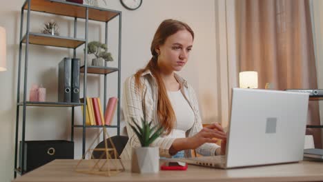 Young-woman-girl-using-laptop-computer-sitting-at-table-working,-online-shopping-from-home-office