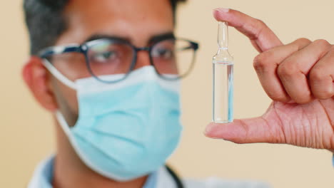 Indian-doctor-man-in-medical-mask-holds-an-ampoule-of-vaccine-medicine-treatment-injection-analyzing