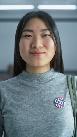 Woman-stands-in-a-modern-polling-station,-poses,-smiles-and-looks-at-camera.-Portrait-of-Muslim-woman,-United-States-of-America-elections-voter.-Background-with-voting-booths.-Concept-of-civic-duty.